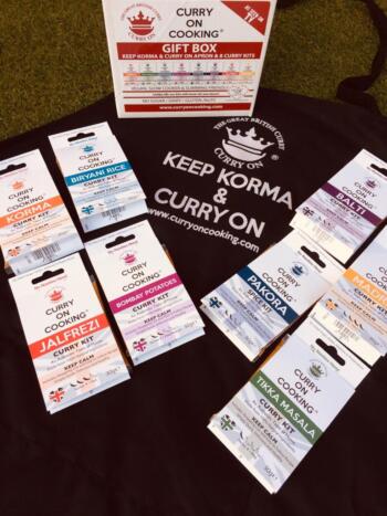 8 Curry On Cooking kits laid on top of a black apron with Keep Korma and Curry On